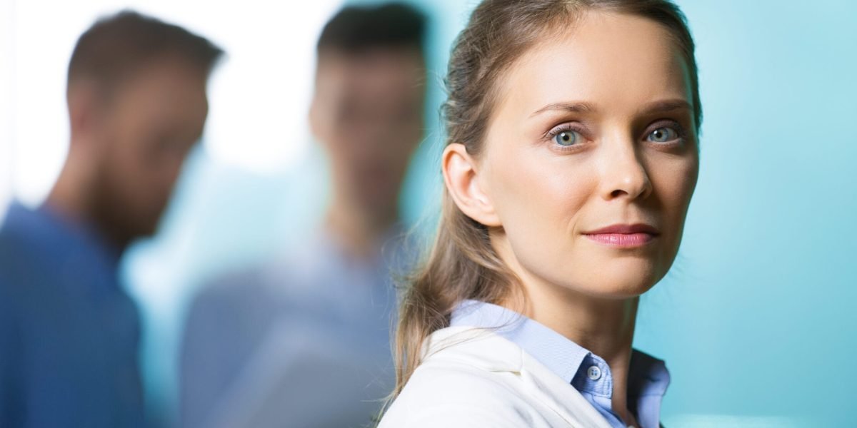 Closeup of serious attractive young woman looking at camera with two blurred men in background